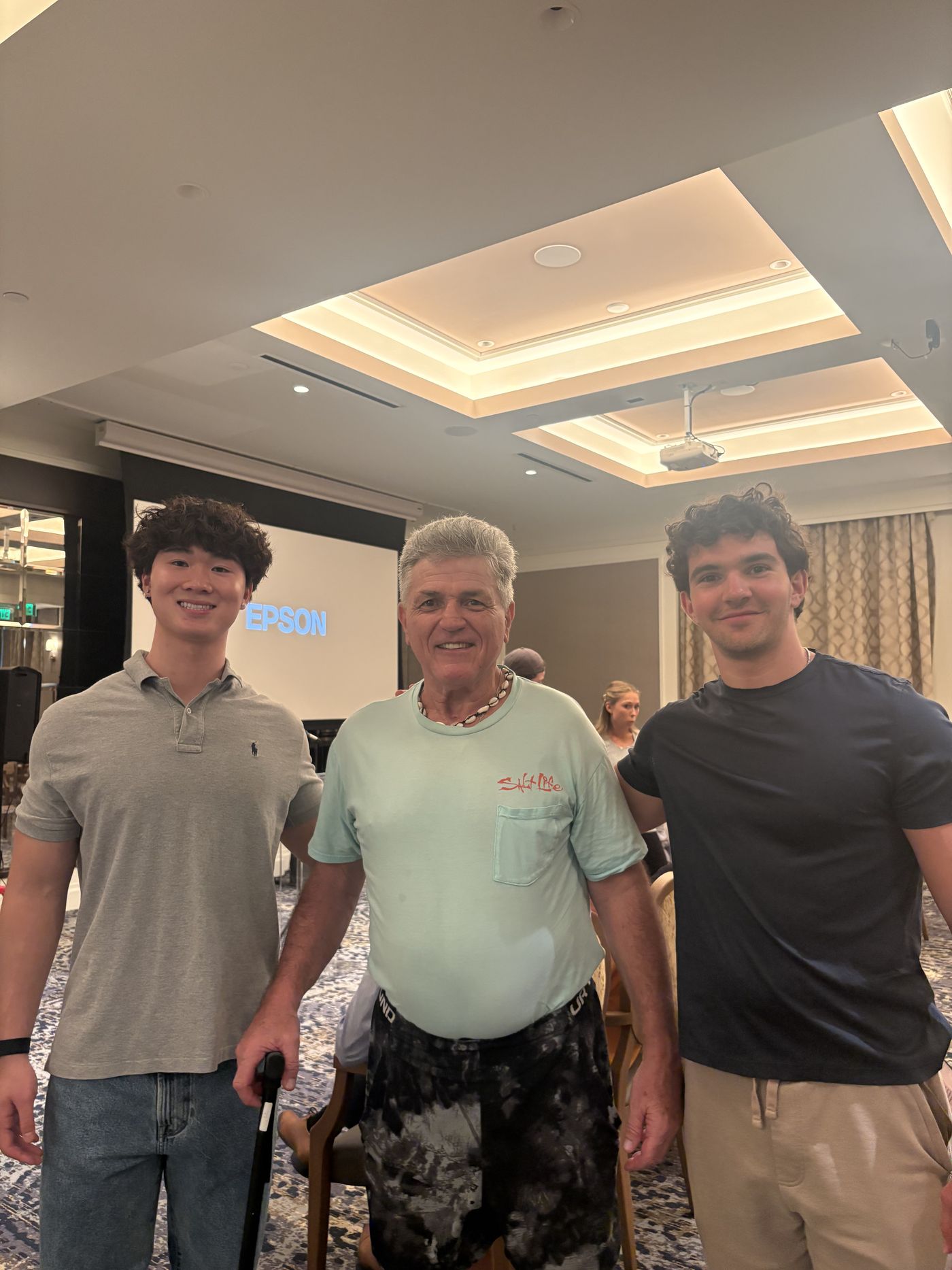 Two Tech Connect students standing on either side of a smiling older man at a community technology session.